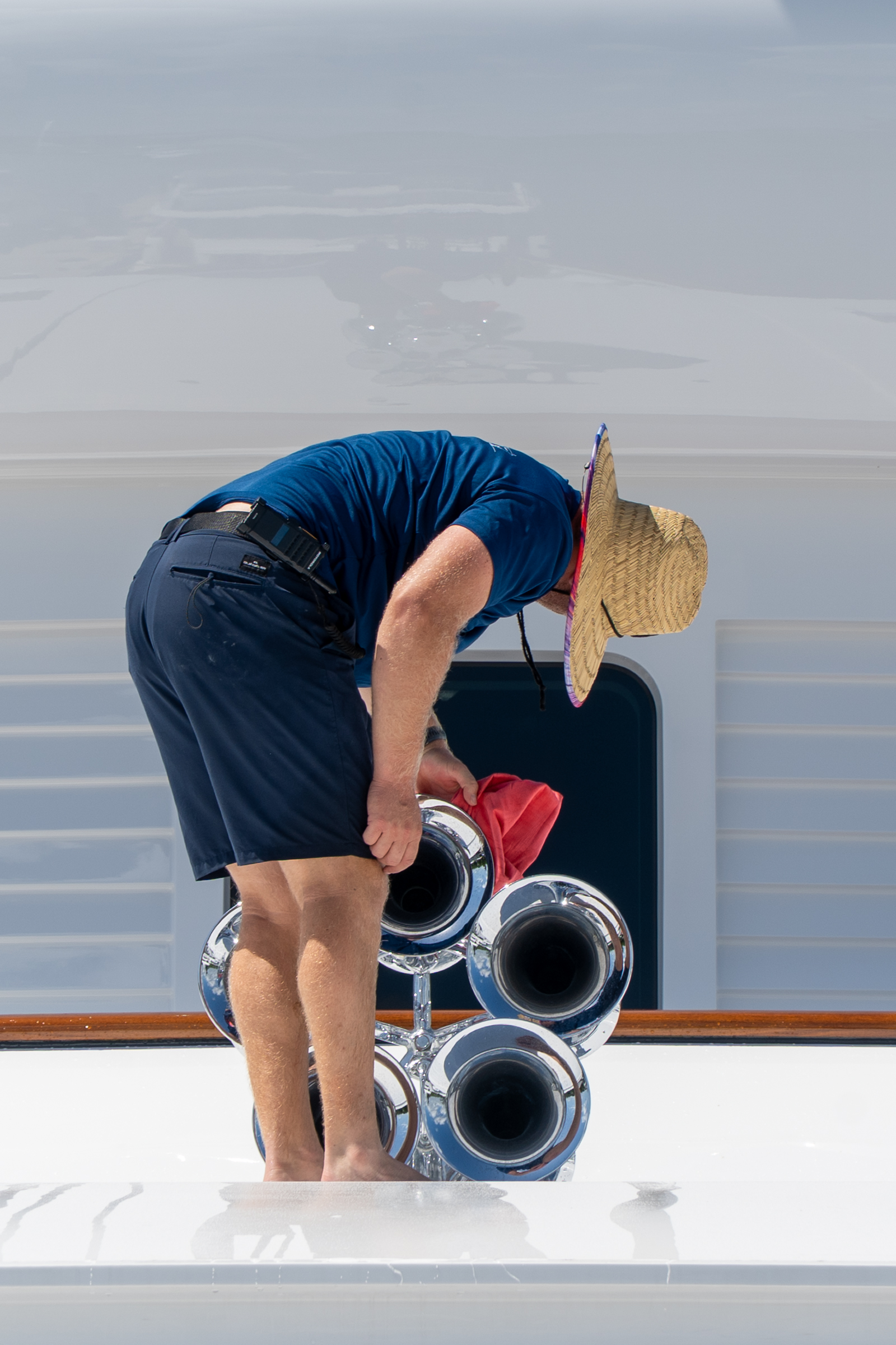 Crew member detailing yacht exhaust hardware on the upper deck